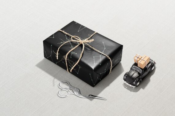 A black Christmas gift box with a pair of scissors waiting to be wrapped in Constellation Wrapping Paper.