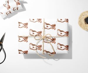 A brown Staffordshire Bull Terrier wrapping paper and scissors next to a Christmas wrapping paper.